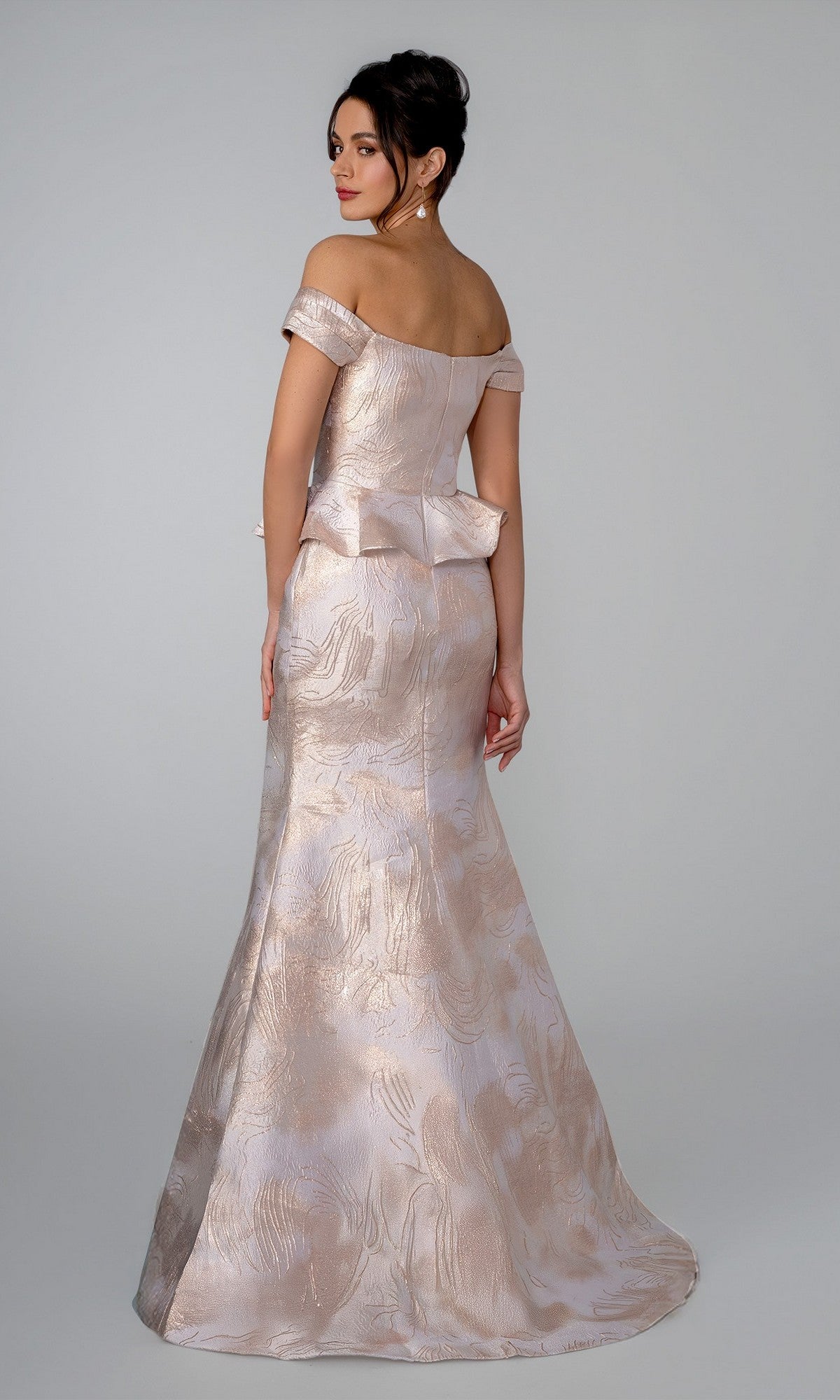 A woman stands against a plain background wearing the Stella Couture 26305, an off-the-shoulder, floor-length light pink gown featuring a subtle pattern, sweetheart neckline, peplum detail, and a mermaid silhouette.